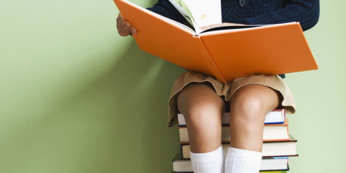 Girl sitting on a tower of books reading